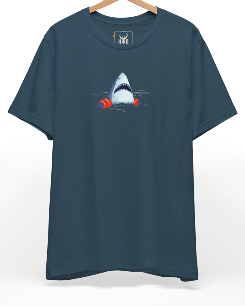 A high-end display of the official Holydeer Shark Graphic Tee showcasing unique Ocean Humor Apparel design lines. The central Cute Shark Clothing graphic features a miniature Nautical Streetwear layout centering a detailed shark head with sharp teeth wearing bright orange Shark Floaties Tee arm bands printed squarely on premium deep teal fabric.