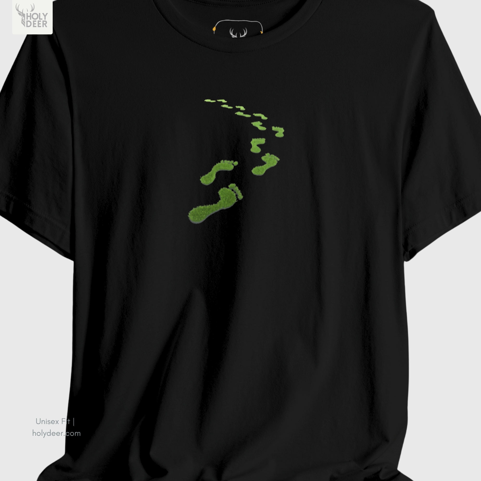 A technical macro view of the Holydeer Tee Green Steps Shirt capturing the tiny shrinking foot particles and desaturated green dust graphics winding towards the top horizon. The frame monitors the clean graphic structure to secure high minimalist green tee layout cohesion, creating a premium presentation for our signature line.