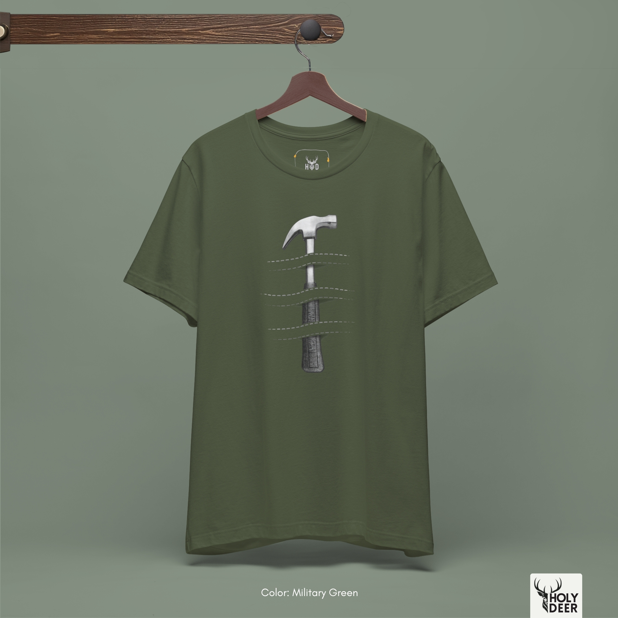 A full-length street fashion lookbook photo displaying a creator styling the Holydeer Apparel Hammer Graphic Tee. The model pairs the independent boutique studio wear and carpentry shirt with loose casual gray utility pants and workshop tools inside a raw minimalist brutalist concrete architectural hall.