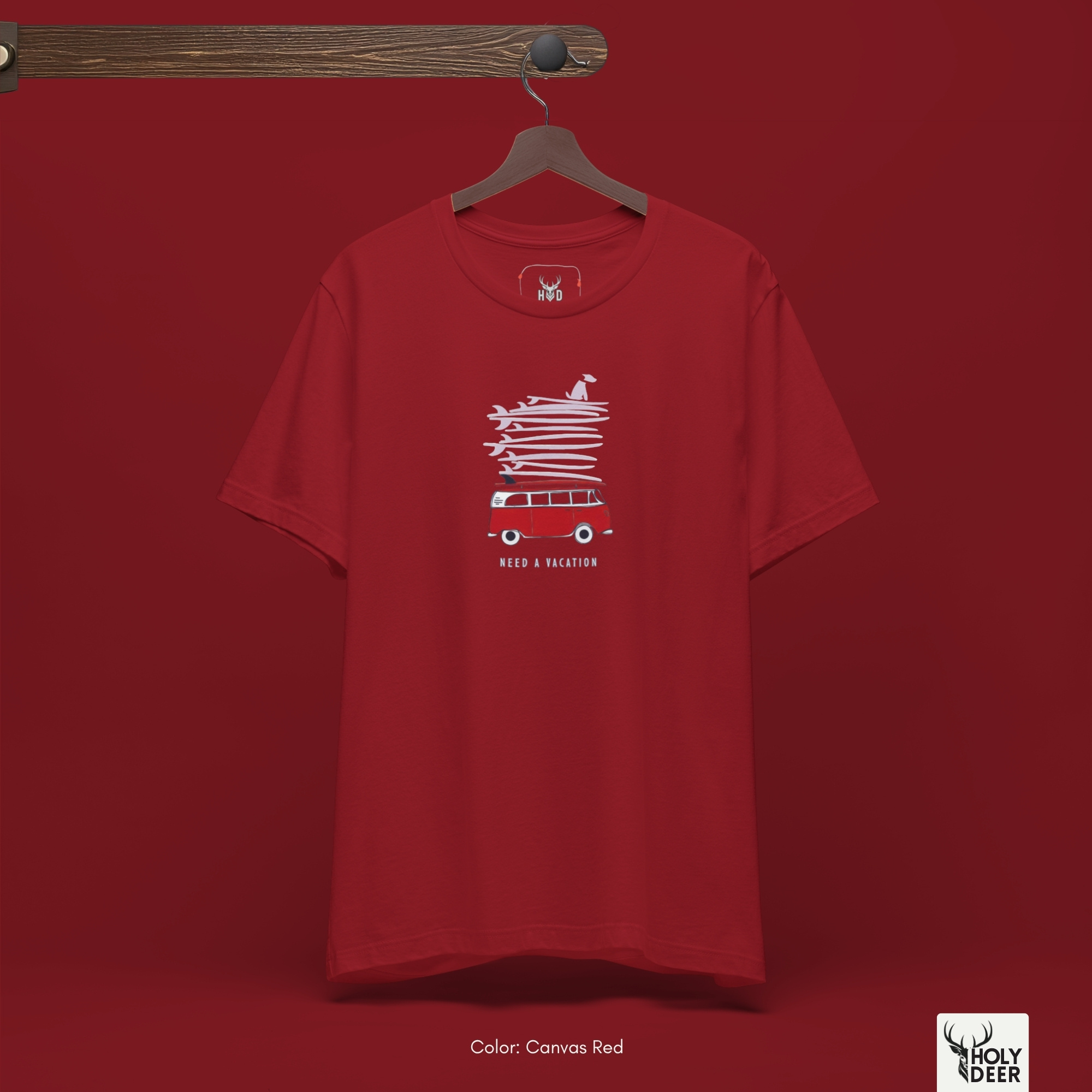 A technical macro view of the Holydeer Tee Vacation Graphic Tee capturing the tiny surfing dog clothing silhouette sitting at the absolute top of the surfboard pile. The frame tracks the clean block typography aligned perfectly underneath the red camper base to secure high ocean humor apparel layout structure.