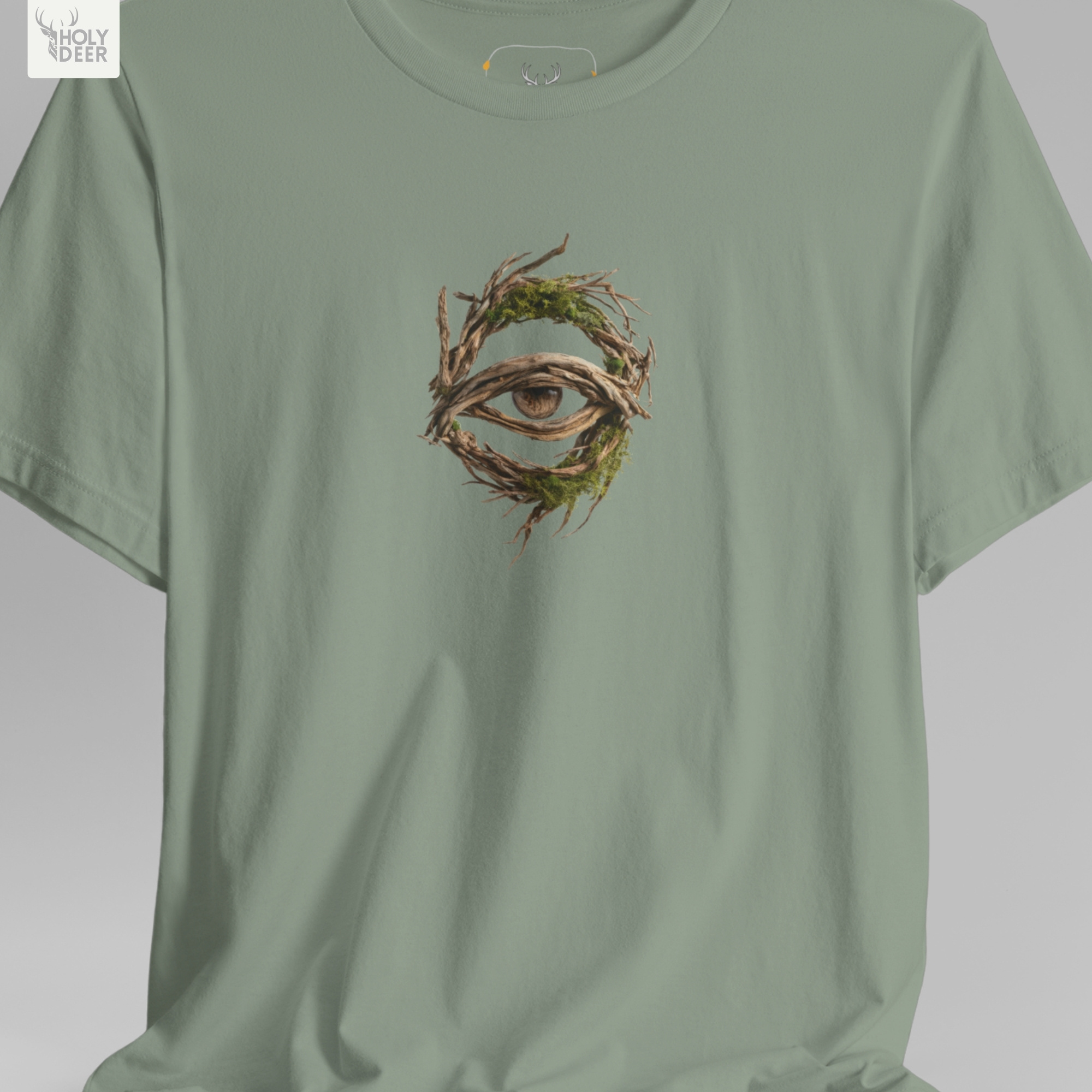 A technical macro view of the Holydeer Tee Forest Eye Shirt capturing the tiny floating leaf particles and desaturated forest dust graphics surrounding the central eye block. The frame monitors the clean graphic structure to secure high eerie nature t layout cohesion, creating a premium presentation for our signature line.