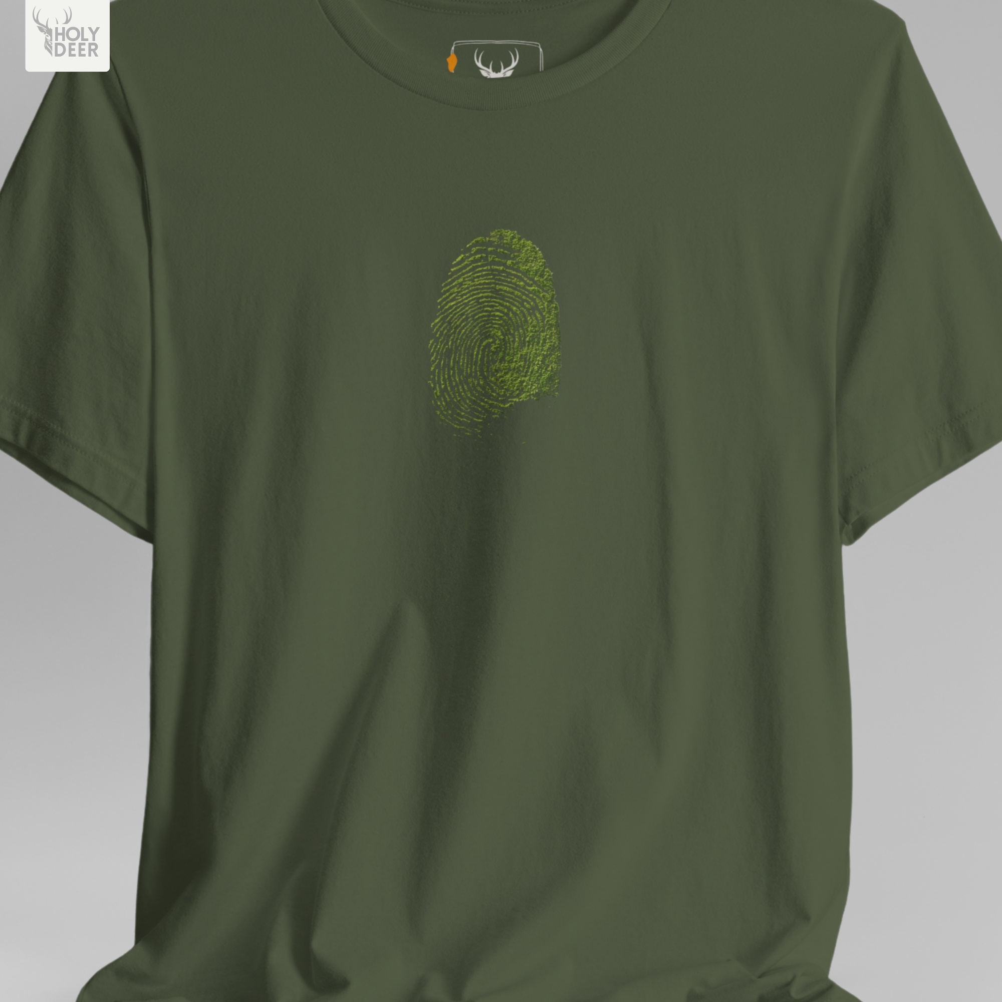 A commercial catalog layout tracking the Holydeer Clothing Green Identity Tee hanging cleanly from a custom timber stand. The product framework documents accurate green living t-shirt material behavior, soft chest wrinkles, and balanced square casual fit parameters for high-end boutique distribution.
