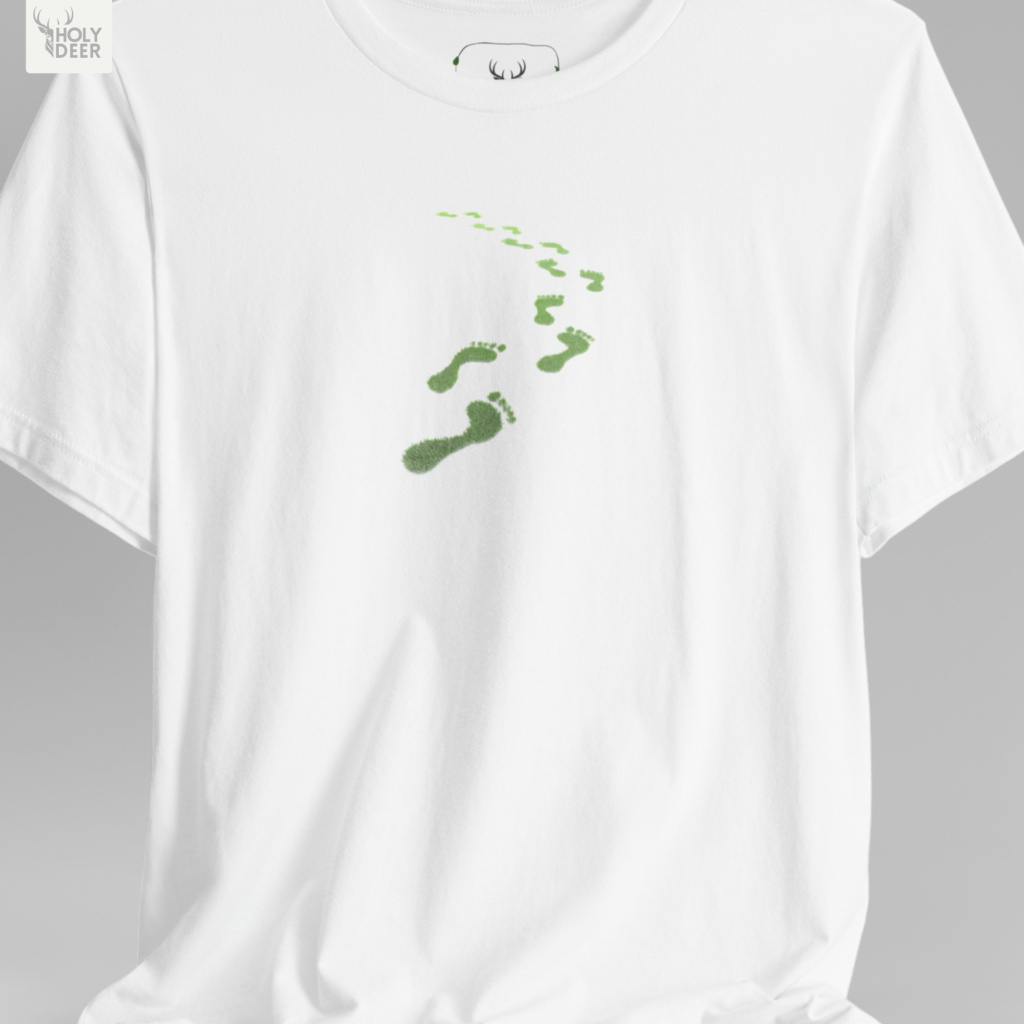 An overhead creative flat lay arrangement displaying the Holydeer Tee Green Steps Shirt folded neatly next to raw styling elements. The merchandise is grouped zekice with deep black shungite mineral stones, actual preserved green moss patches, raw hemp coordinates, and alternative leaf footprints tee lookbook magazines.